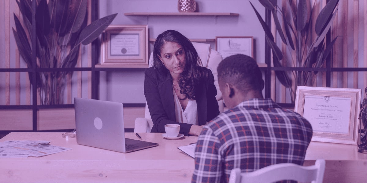 A imagem retrata um encontro formal em um escritório, onde uma advogada está conversando com um cliente. A cena transmite seriedade e profissionalismo, com documentos e um laptop sobre a mesa, sugerindo uma consulta jurídica. No fundo, diplomas emoldurados reforçam a credibilidade da profissional. Esta imagem pode estar relacionada à "Gratuidade de justiça e art. 98 do CPC", que assegura o benefício da justiça gratuita àqueles que comprovarem insuficiência de recursos para arcar com as custas processuais, abrangendo taxas, despesas com provas e honorários periciais, permitindo o acesso à justiça sem comprometer a subsistência da parte.