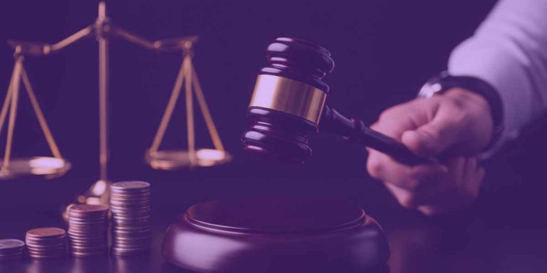 A imagem mostra uma balança da justiça ao lado de pilhas de moedas e um martelo de juiz sendo segurado,