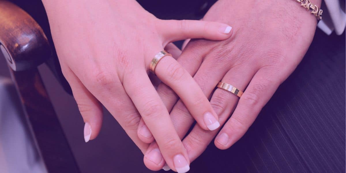 Um casal com as mãos juntas e alianças de casamento no dedo, simbolizando a comunhão universal de bens.