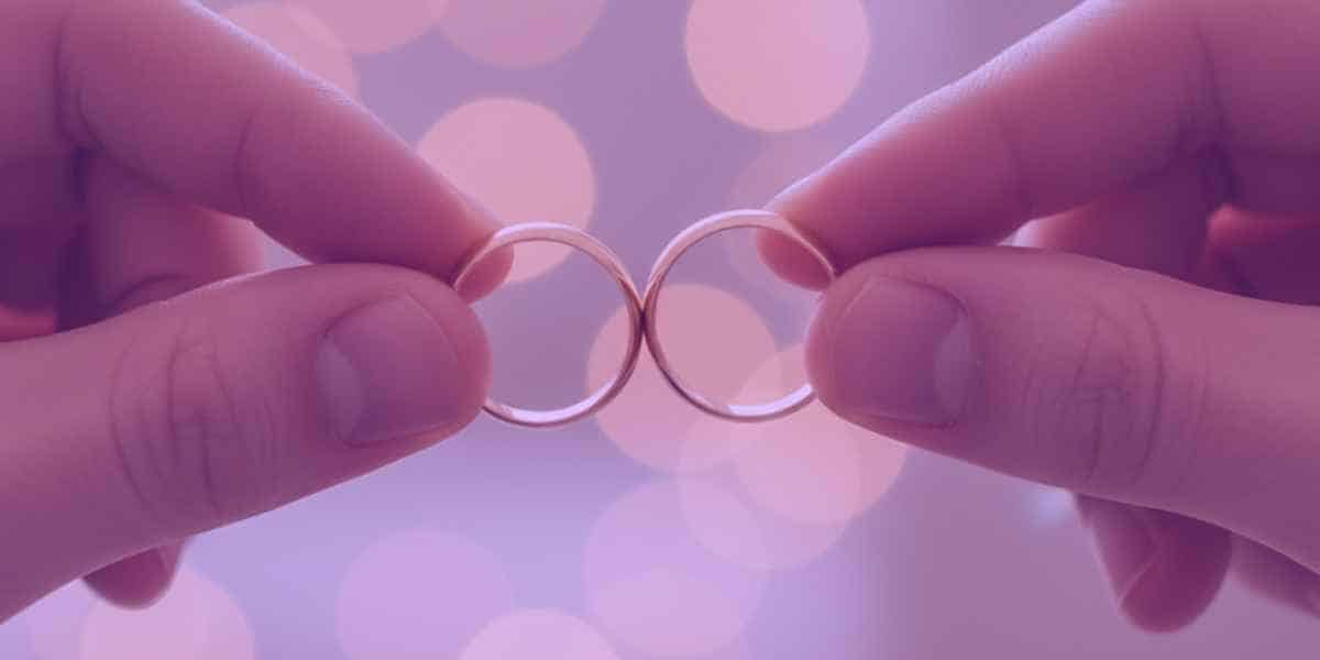 Um casal segurando as alianças de casamento, simbolizando a comunhão parcial de bens.